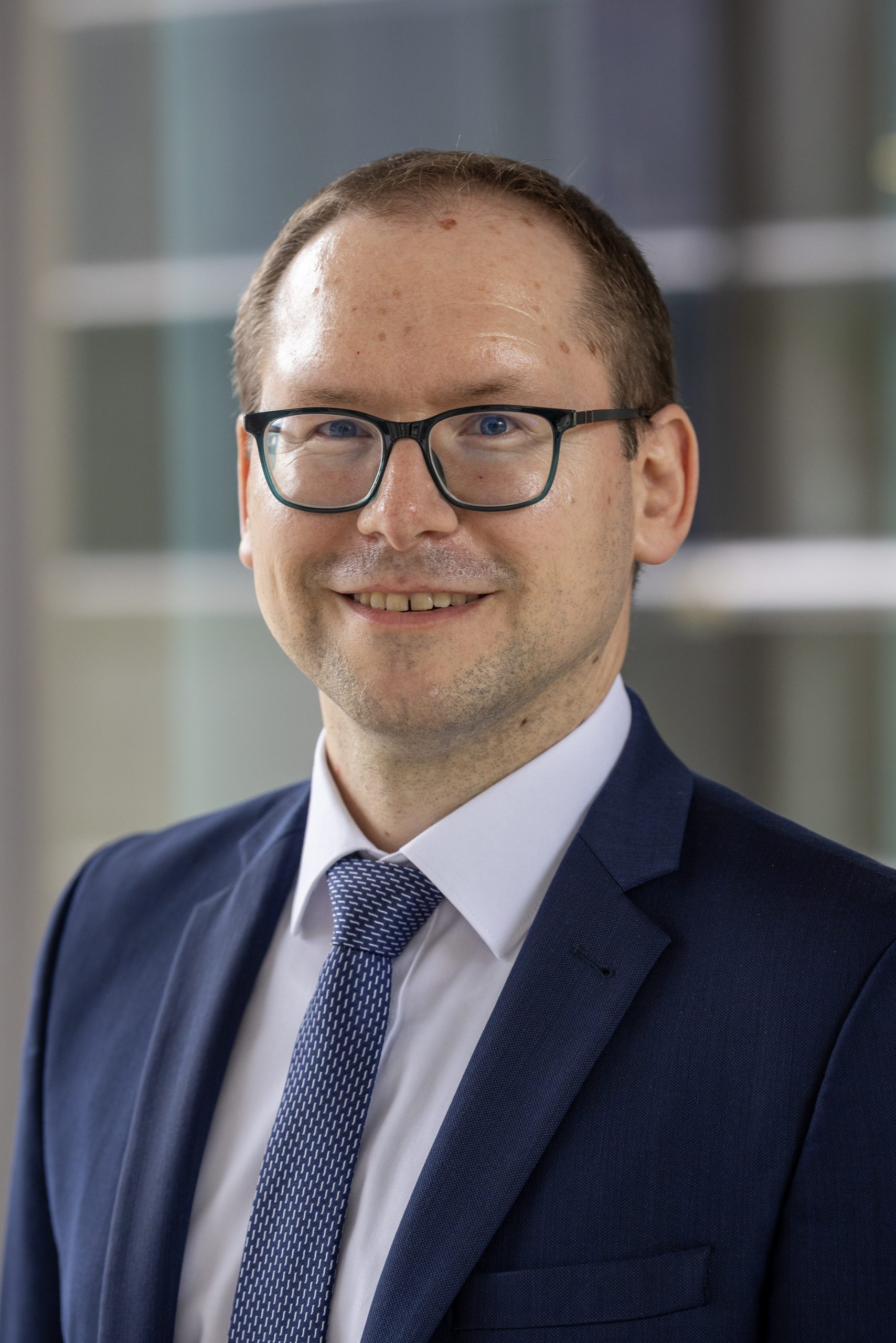Person trägt eine Brille, einen Anzug, ein weißes Hemd und eine Krawatte mit Schnittmuster.