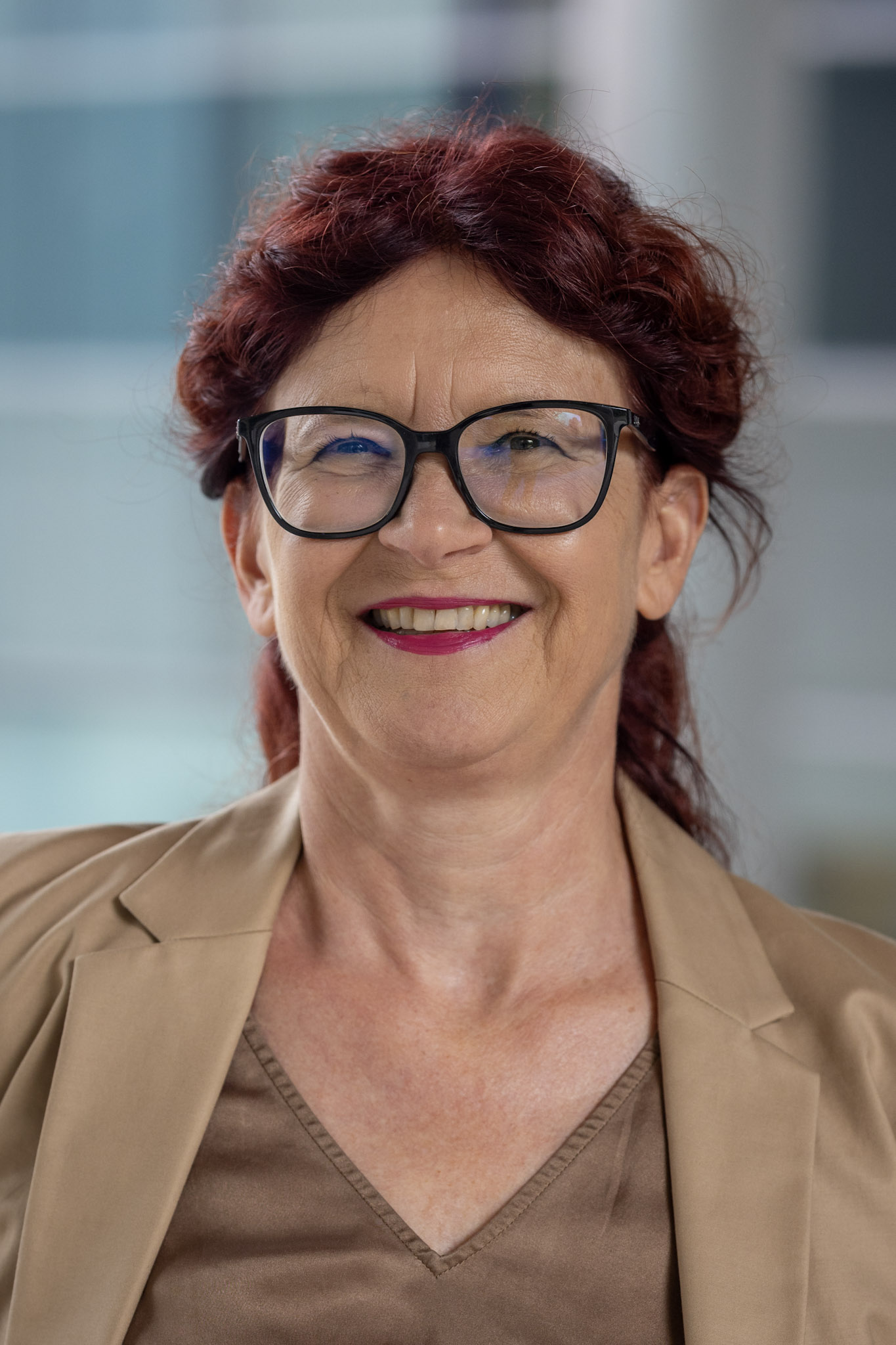 Eine Person, die eine Brille und einen Blazer trägt, lächelt in die Kamera.