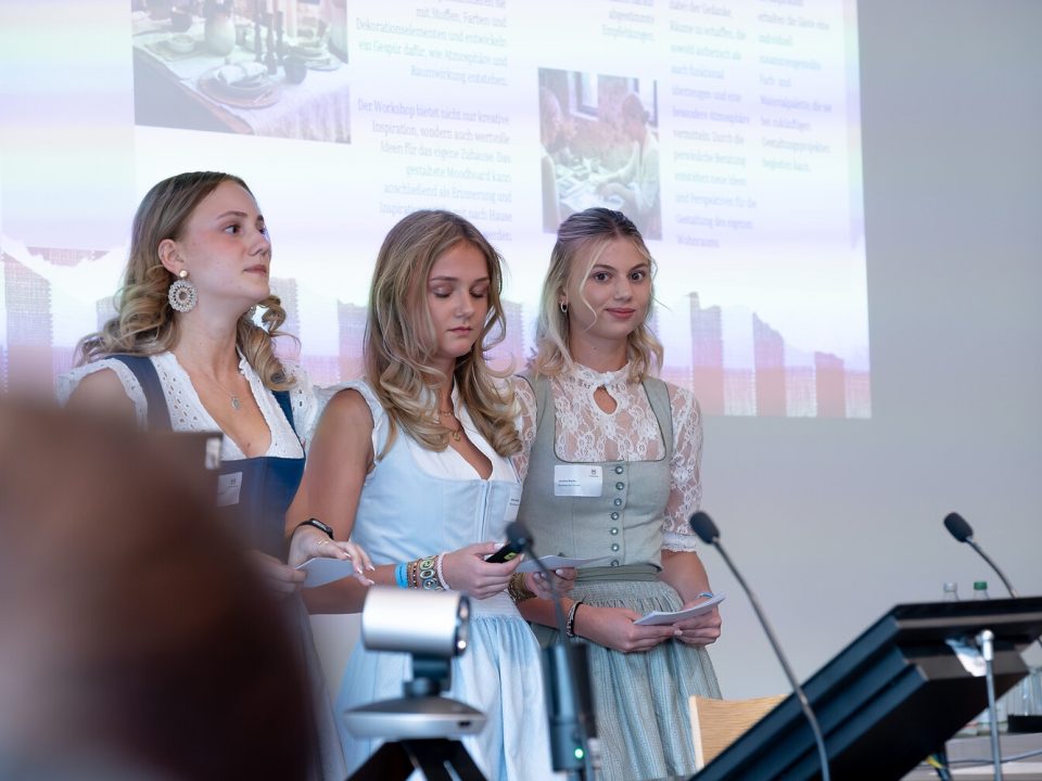 Drei Personen in traditioneller Tracht stehen mit Mikrofonen im Vordergrund und konzentrieren sich auf das Hauptprodukt oder die Idee, um die es gerade geht.