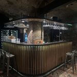 Moderne Bar mit Holzlatten, hängenden Gläsern, Metallhockern und einem Weinkühlschrank.