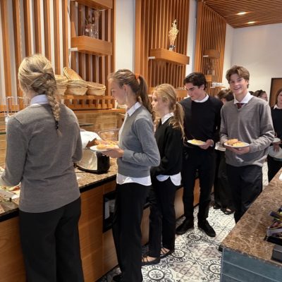 Menschen in Uniform stehen mit Tabletts an der Theke einer Selbstbedienungscafeteria Schlange und suchen sich Speisen aus.