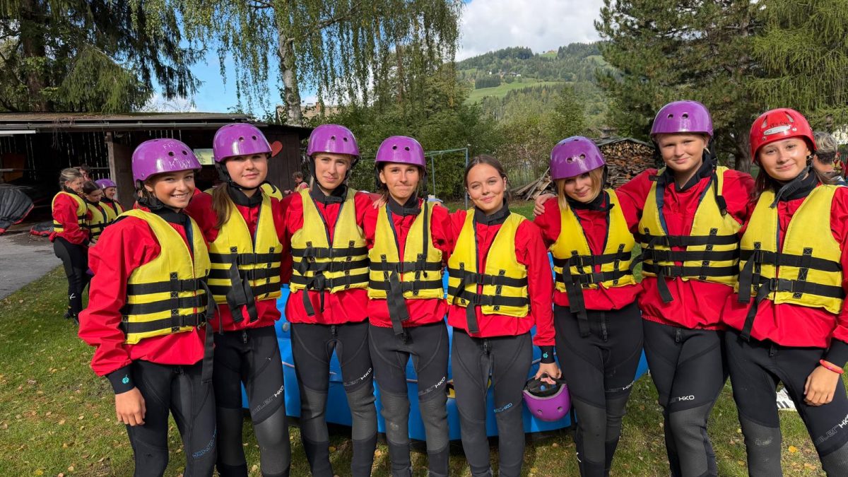 Eine Gruppe von Menschen, die Schwimmwesten und Helme tragen, steht beieinander und bereitet sich auf eine Wasseraktivität vor.