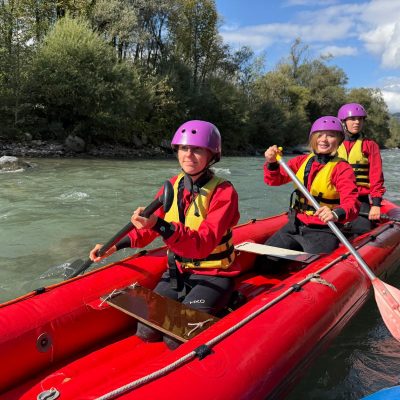 Menschen, die mit Helmen und Schwimmwesten bekleidet auf einem Schlauchboot paddeln.