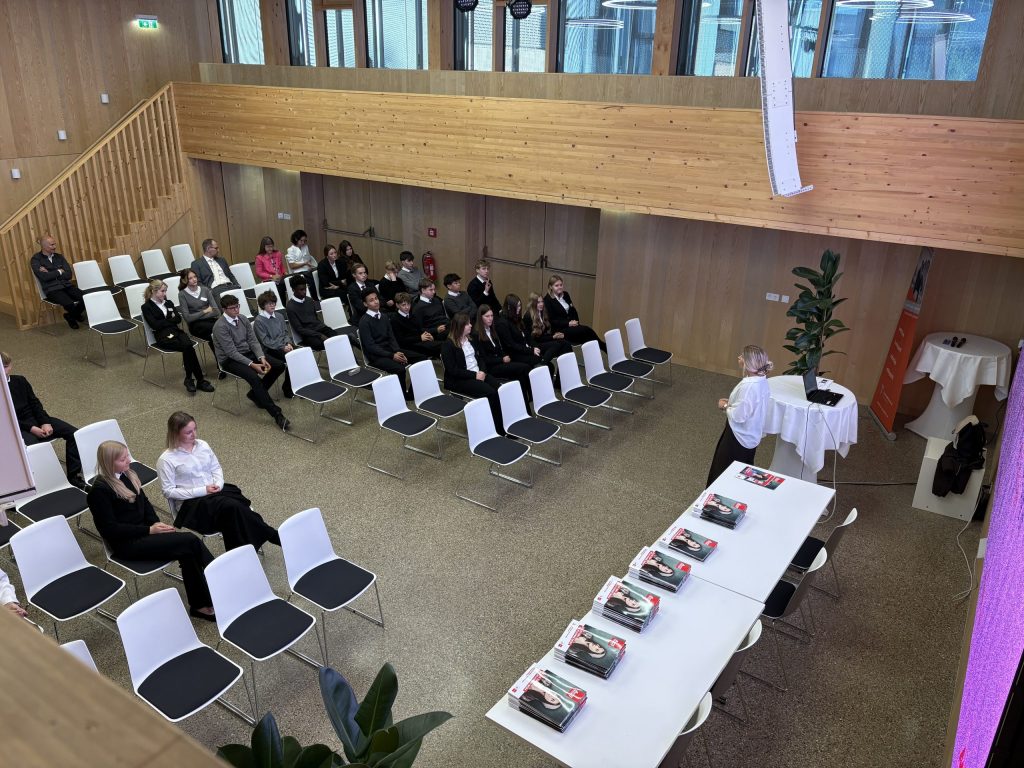 Schülerinnen und Schüler hören Vortrag in modernem Schulgebäude
