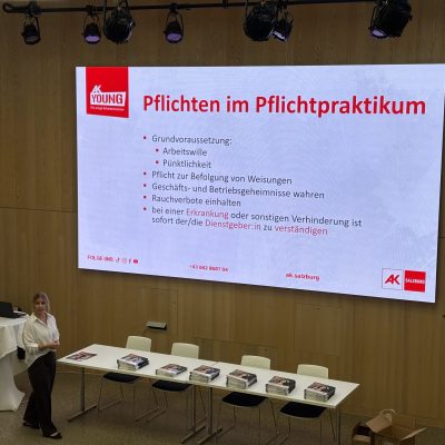 Es ist ein Podium mit einer projizierten Folie mit dem Titel „Pflichten im Pflichtpraktikum“ zu sehen.