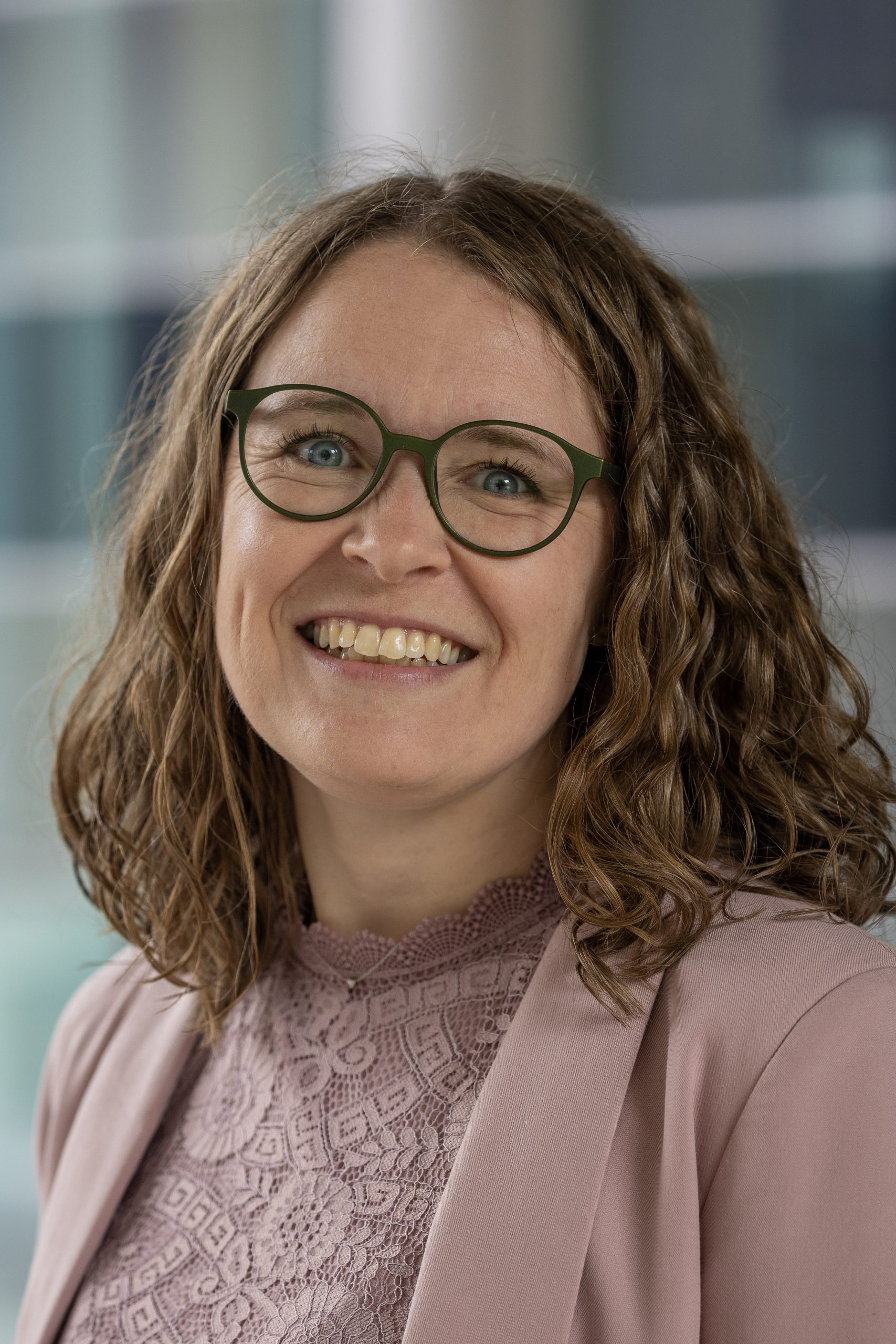 Lächelnde Person, die eine Brille und ein Spitzenoberteil mit einem Blazer trägt.