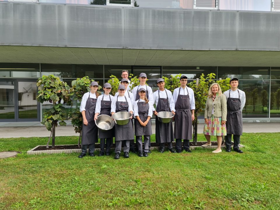 Personen in Kochuniformen und Schürzen halten Rührschüsseln in den Händen; zu ihnen gesellen sich zwei weitere Personen in Alltagskleidung. Der Fokus liegt auf den Rührschüsseln.