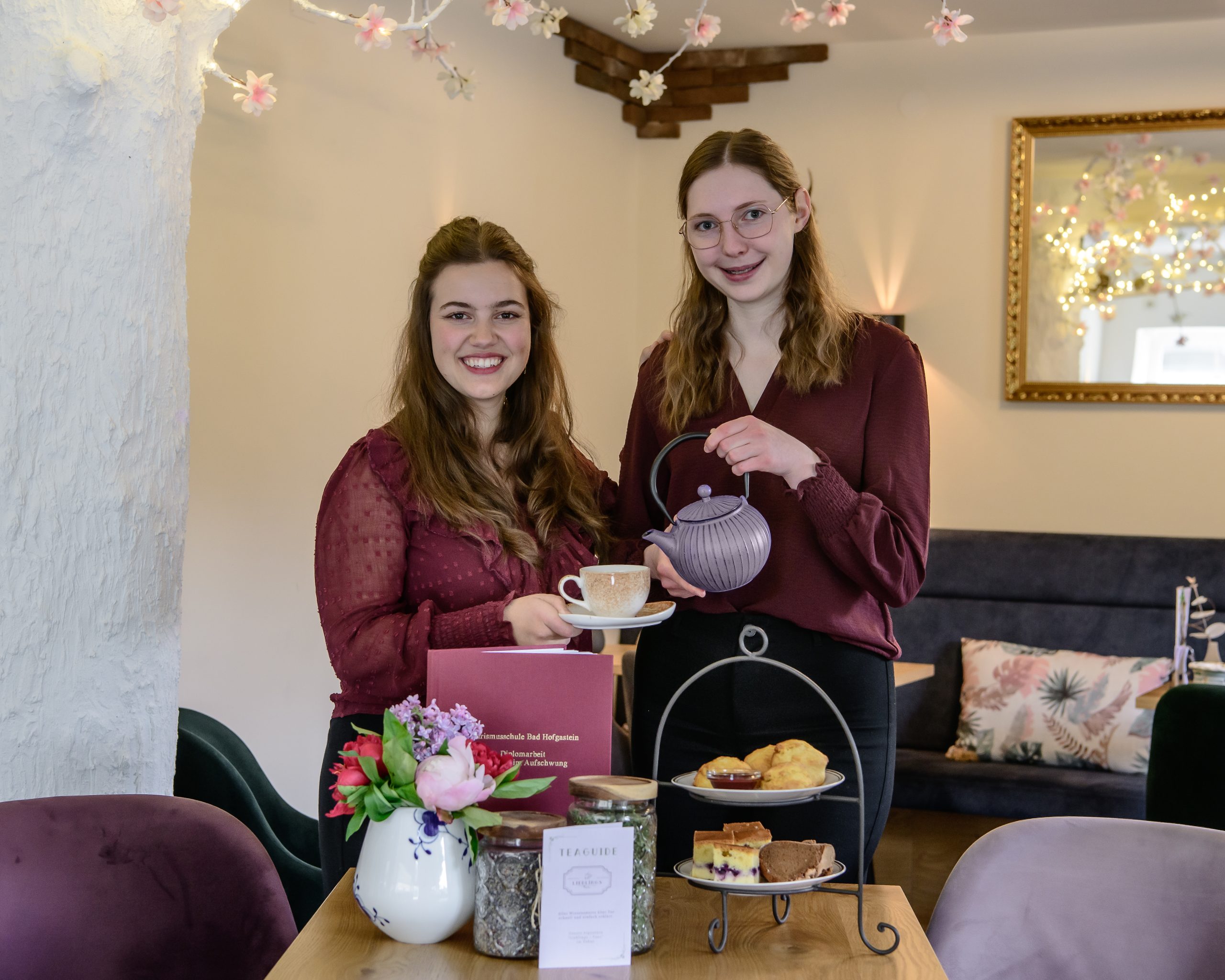 Teetasse, Untertasse und Teekanne, die an einem mit Kuchen und Scones gedeckten Tisch benutzt werden. Teetasse, Untertasse und Teekanne, die an einem mit Kuchen und Scones gedeckten Tisch benutzt werden.