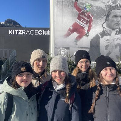 Gruppe in Winterkleidung in der Nähe eines Plakats mit dem Thema Hahnenkammrennen Kitzbühel.