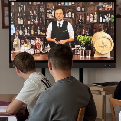 Die Menschen in einem Raum sehen auf einem großen Bildschirm eine Präsentation zur Herstellung von Cocktails.