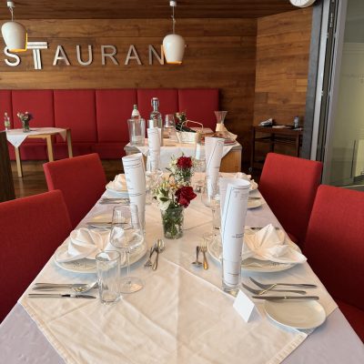 Ein Restauranttisch mit gefalteten Servietten und einem Blumenschmuck, ideal für die Feier der Vorprüfungen der Reife- und Diplomprüfungen 2025.