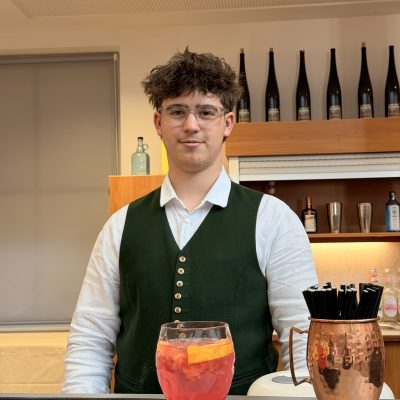 Eine Person hält einen Cocktail in der Hand und ist bereit, über die Vorprüfungen für die Reife- und Diplomprüfungen 2025 zu diskutieren.
