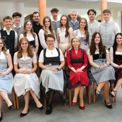 Gruppenfoto, auf dem fünf Personen in der vorderen Reihe die Maturaklasse und die Abschlussklasse 2025 repräsentieren; die meisten tragen traditionelle Kleidung.