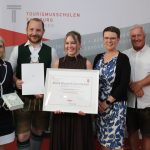 Fünf Personen bei einer Preisverleihung, in deren Mitte eine Urkunde für die Maturaklasse und Abschlussklasse 2025 ausgestellt ist.