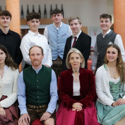 Eine Gruppe in traditioneller Tracht, die die Maturaklasse und die Abschlussklasse 2025 repräsentiert; einige stehen, andere sitzen.