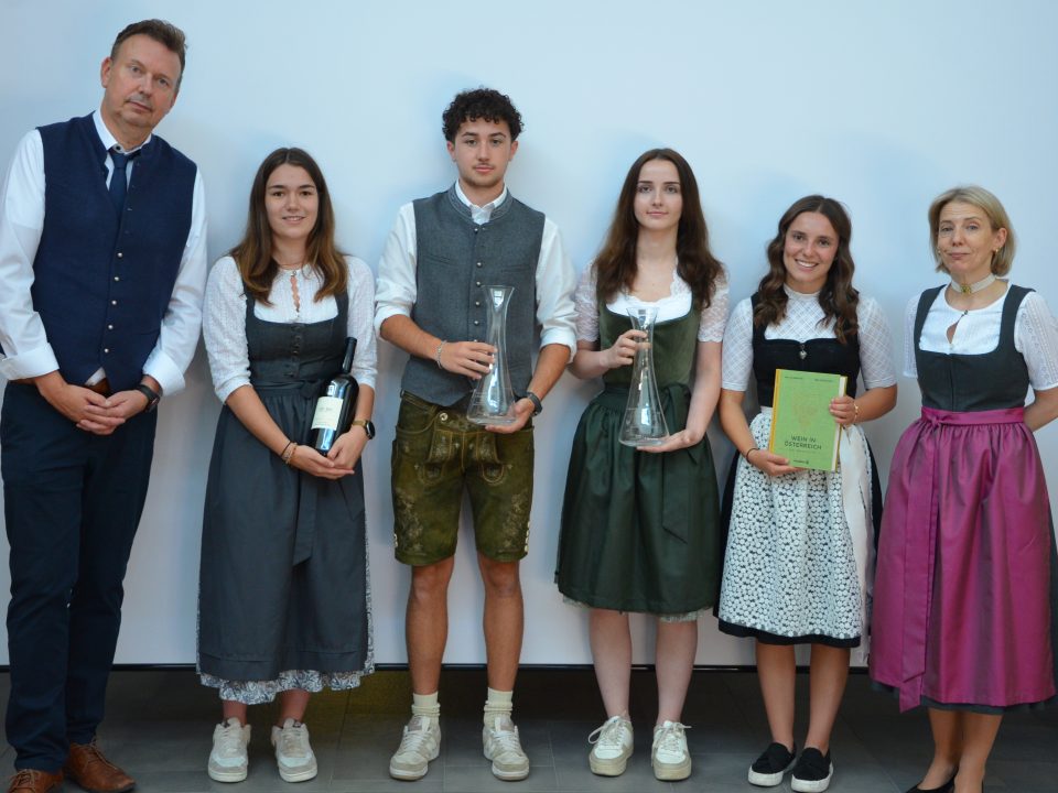 Sechs Personen, darunter die Gewinner des Wettbewerbs „Jungsommelier Österreich 2019“, stehen gemeinsam in traditioneller Tracht da, wobei vier von ihnen Auszeichnungen in den Händen halten.