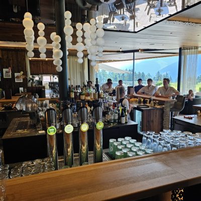 Bar mit Zapfhähnen und Gästen vor Panoramafenstern mit Bergblick